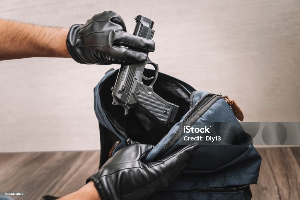 man in gloves takes a gun out of his backpack. Seizure of weapons and baggage search. Crime concept. The policeman searches the bag. evidence of a crime. A man in gloves takes a gun out of his backpack. Seizure of weapons and baggage search. Crime concept. The policeman searches the bag. evidence of a crime. Weapon Stock Photo