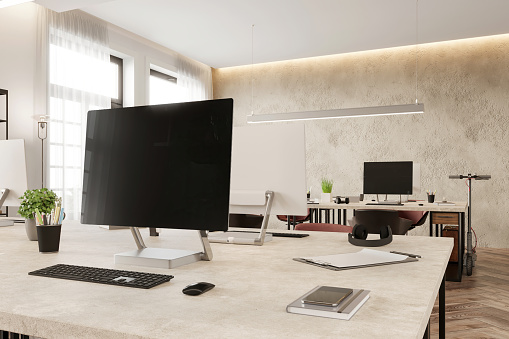 Large blank monitor with keyboard and office supplies on desk. Modern office in the background. Render