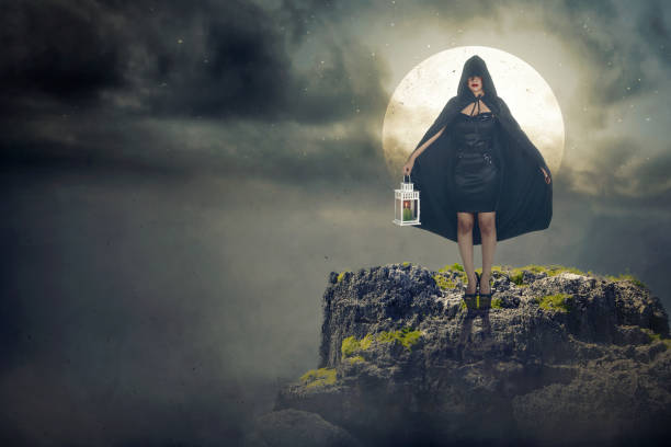 Asian witch woman with a black cloak holding a lantern standing on the stone with a night scene background
