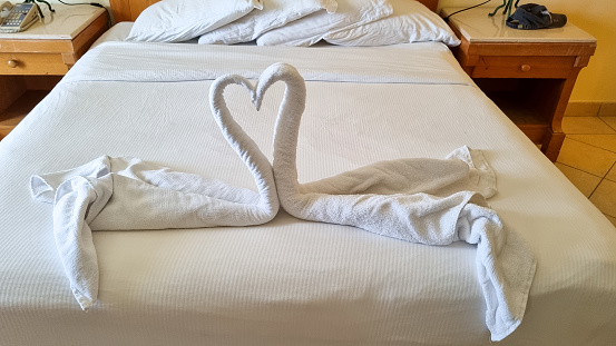 Folded from a white towel swan on the bed in the hotel room. Traditional decoration of the rooms of the hotel guests when cleaning the rooms.
