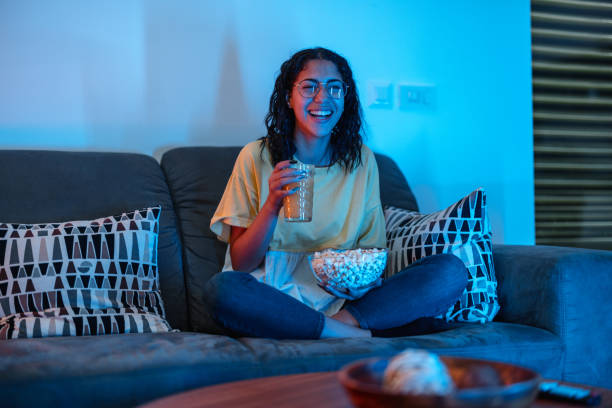 istock Young Hispanic Female Laughs Hard While Watching TV Show. She Drinks Orange Juice And Holds Popcorn 1433072940