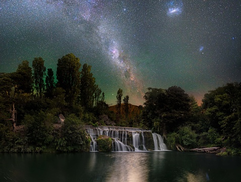 The beautiful view of a waterfall and green vegetation with Milky Way in the background. New Zealand.