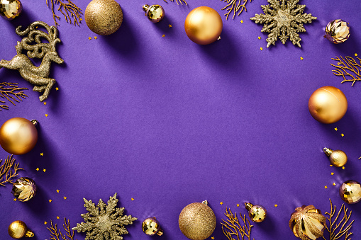 Elegant Christmas composition. Flat lay gold baubles, decorations, confetti on purple background. New Year postcard design, Xmas banner template.