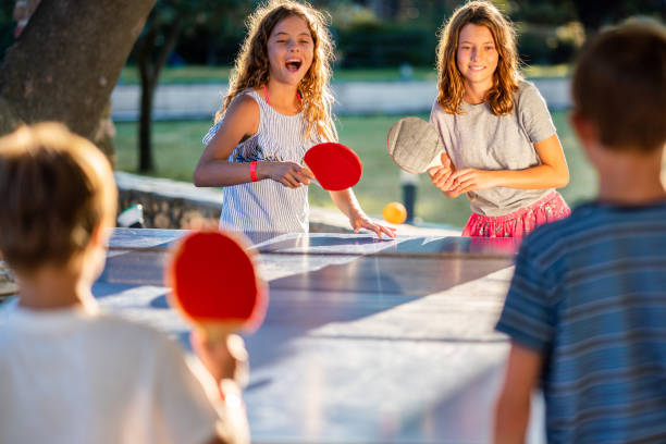 Happy group of children playing table tennis on summer day