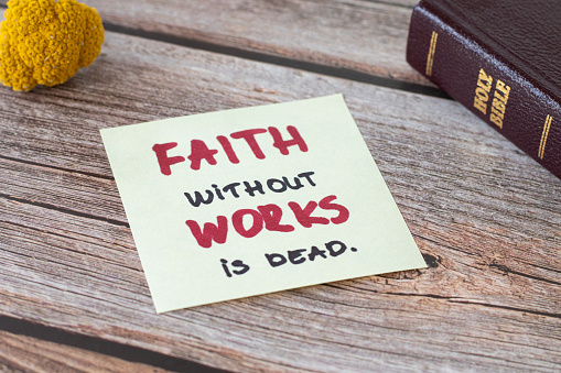 La fe sin obras está muerta, una nota bíblica escrita a mano y un Libro Bíblico Santo cerrado sobre una mesa de madera photo