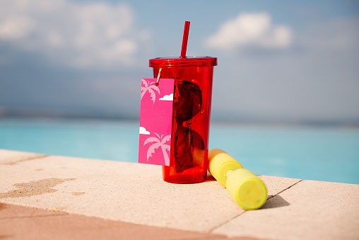 A concept of summer holidays- a red glass with sunglasses on a sea background