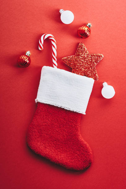 istock Christmas stocking with striped candy cane, star decoration, baubles on red background. Christmas Santa Claus socks. Winter holidays celebration concept. 1433080900