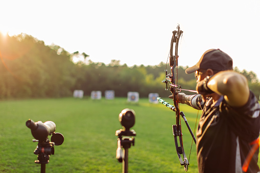 Man with prosthetic arm practicing archery with compound bow on the field doing his training at sunset.