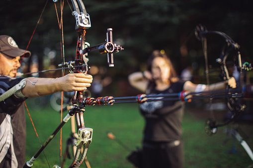 Man and woman with prosthetic arms practicing archery with compound bow on the field on training.