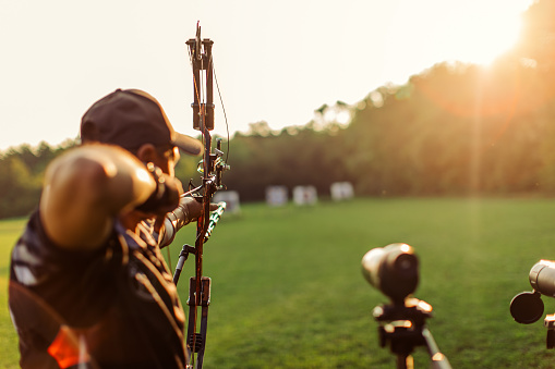 Man with prosthetic arm practicing archery with compound bow on the field doing his training at sunset.