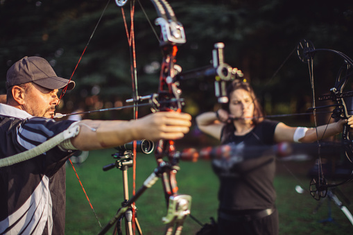 Man and woman with prosthetic arms practicing archery with compound bow on the field on training.