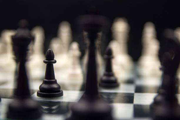 istock Selective focus of a black pawn among white and black chess pieces on a board on dark background 1433082937