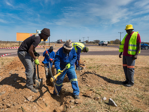 group of African workers in blue workwear and the supervisor using a pick and shovels digging a trench