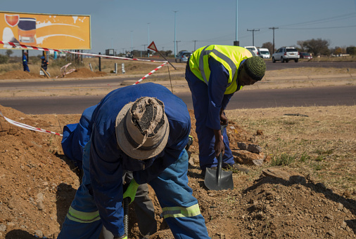 two African workers with reflective vest and hat digging on the side of the road