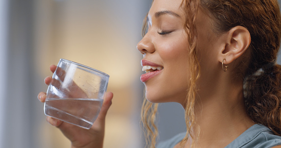 Woman, water and eyes closed with drink in hand to hydrate  body for a healthy lifestyle routine. Young person enjoying aqua hydration for mind wellness and skin wellbeing with an active life.