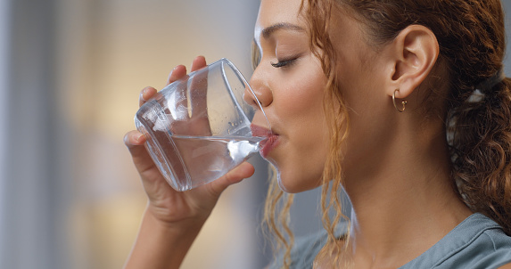 Primer plano de una mujer bebiendo un vaso de agua para hidratación, sed y salud en su casa. Chica feliz con un bienestar, dieta y estilo de vida saludable disfrutando de una bebida acuática fresca mientras se relaja en casa. photo