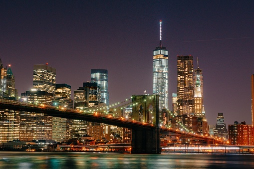 A beautiful shot of the Brooklyn Bridge against skyscrapers of New York illuminated at night