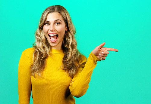 Marketing, mockup and woman pointing to a discount sales deal or offer in a happy, wow and excited studio portrait. Mock up space, smile and young girl showing advertising announcement with finger