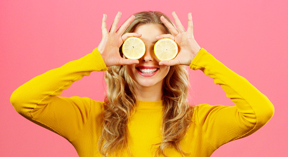 Woman, hands with lemon on eyes and health diet on a studio background. Wellness, food and healthy lifestyle of happy girl with fresh citrus fruits for vitamins, minerals and nutrition with a smile.