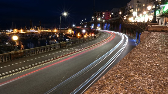 A long exposure shot of a curving road at night with red and blue streaks of traffic surrounded by bright street lamps