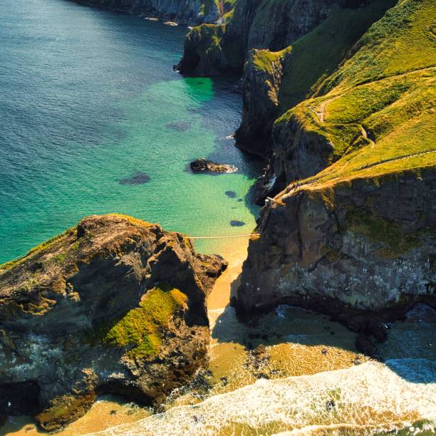 aerial shot of the carrick-a-rede (national trust) rope bridge with a sea connecting two cliffs - national trust northern ireland uk rock imagens e fotografias de stock