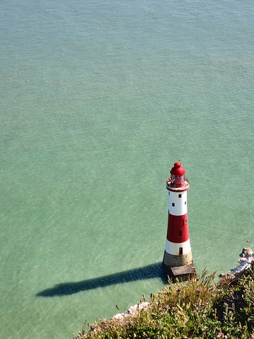 A vertical low angle shot of a lighthouse at Seven Sisters in England with a pale green sea on a sunny day