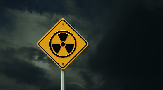 Yellow off road traffic sign with radioactive symbol before dark cloudy sky. Horizontal composition with copy space.