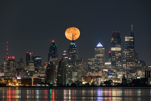 The bright yellow full moon over Philadelphia skyline reflected in the lake at night