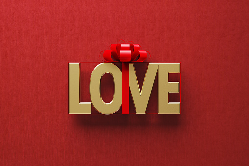 Gold colored love word wrapped by red ribbon on red background. Directly above. Horizontal composition with copy space. Great use for Valentine's Day concepts.