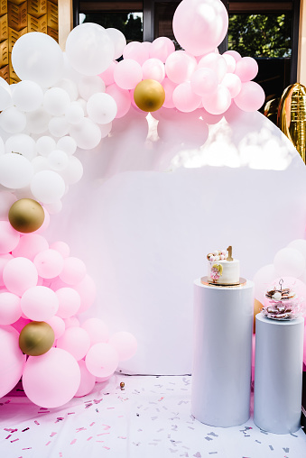 Arch decorated with pink, white and gold balloons. Trendy Cake for a girl. Copy space. Birthday Cake for 1 year on a background photo wall. Delicious reception at a birthday party.