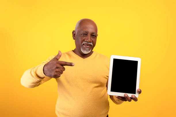 istock Happy senior black man demonstrating digital tablet, pointing at empty screen on orange background, mockup 1433105663