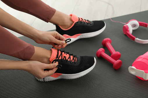 Woman tying sneaker's shoelaces on exercise mat, closeup
