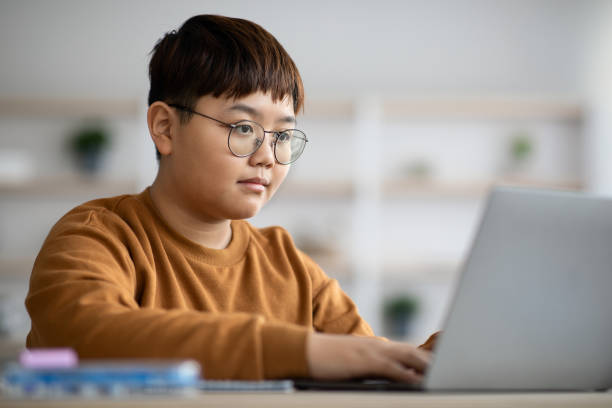 adolescente inteligente sentado frente a la computadora portátil, haciendo la tarea - teen obesity fotografías e imágenes de stock