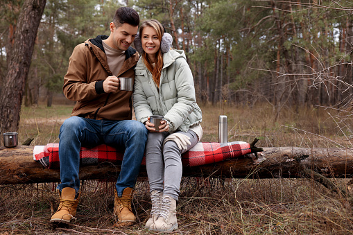 Happy couple with hot drinks spending time together in forest