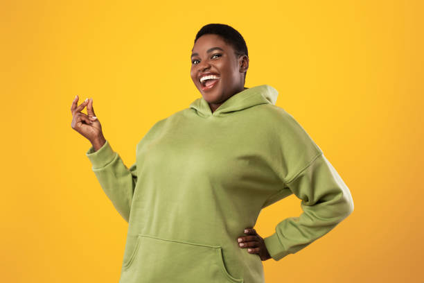 joyful overweight black woman snapping fingers over standing yellow background - snapping imagens e fotografias de stock