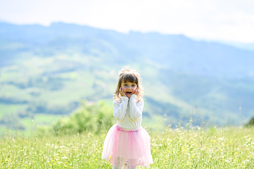 Surprised cute child in a pink dress portrait in a nature with blurred bokeh background and space