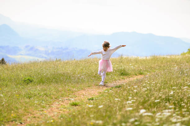 szczęśliwa dziewczynka biegająca po łące. 3-letnia dziewczynka biegnąca z otwartymi ramionami mała szczęśliwa dziewczynka na łące. letnia zabawa na świeżym powietrzu. - mountain mountain peak snow spring zdjęcia i obrazy z banku zdjęć