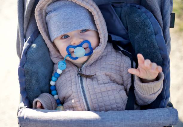 Sweet baby boy with blue eyes, looking at the camera, rising left hand, smiling Adorable baby boy with blue eyes sitting inside his pram outdoors baby stroller winter stock pictures, royalty-free photos & images