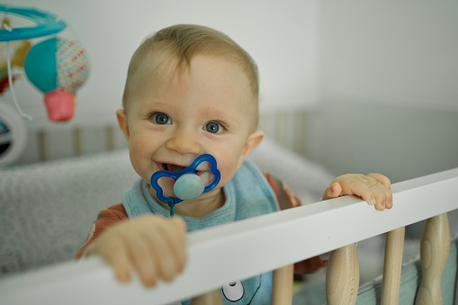 Baby boy with blue eyes standing in cot, close up