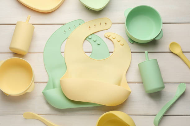 istock Flat lay composition with silicone baby bibs and plastic dishware on white wooden background 1433116452