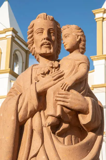 Orange colored statue of Saint Joseph with child Jesus in front of Mission San Jose del Cabo in Mexico