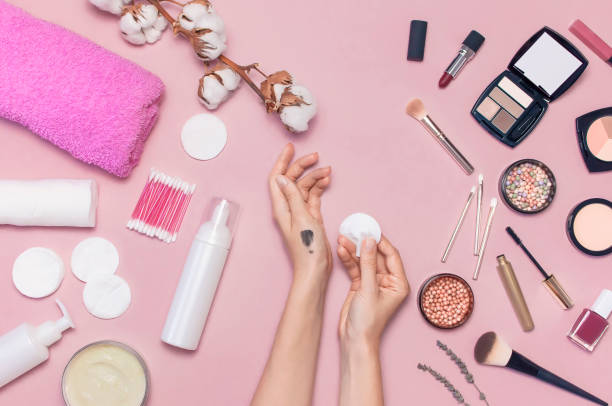 istock Make-up Remover Accessories. Flat lay background Womens hands try cosmetics, cotton branch, cotton pads, cosmetic bottle containers, pink towel, various make-up cosmetics, mascara, powder, lipstick, eyeshadow 1433118160