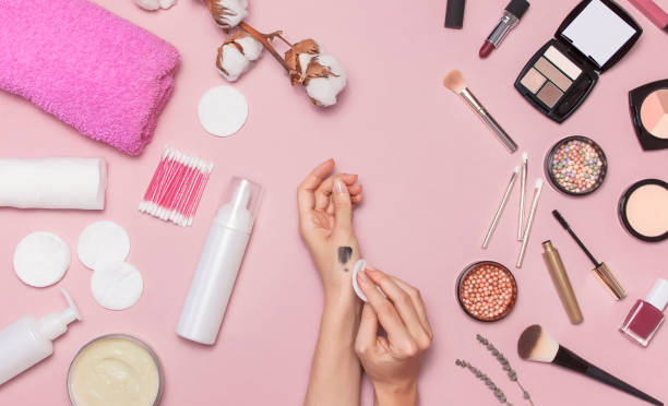 istock Make-up Remover Accessories. Flat lay background Womens hands try cosmetics, cotton branch, cotton pads, cosmetic bottle containers, pink towel, various make-up cosmetics, mascara, powder, lipstick, eyeshadow 1433118163
