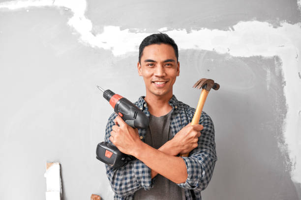 A young Asian man smiles while holding drill and hammer for home DIY improvement stock photo