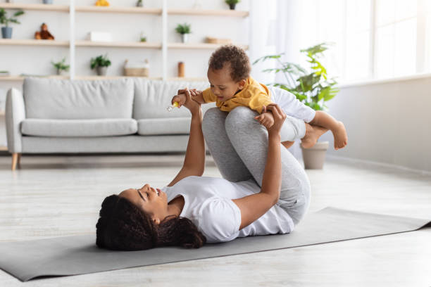 attività sportive con baby. mamma nera che esercita con il figlio neonato a casa - african ethnicity exercising muscular build healthy lifestyle foto e immagini stock