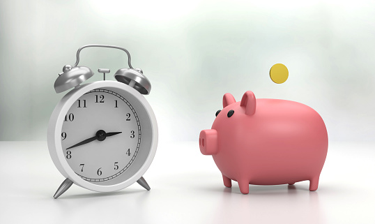 Alarm clock on the table and piggy bank filled with coin. Saving Money Concept.