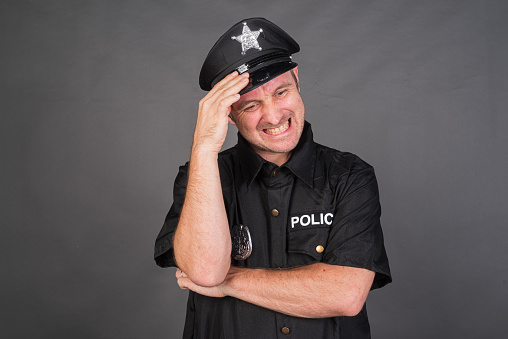 Frustrated Caucasian man wearing police uniform costume against gray studio background