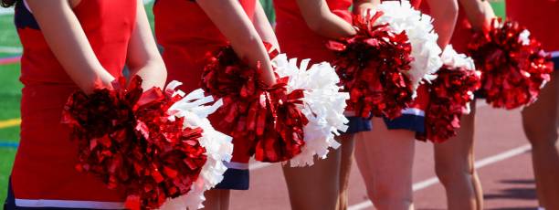 istock Cheerleaders standing on the sideline holding pom poms behind them 1433123980