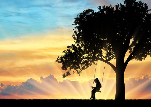 Silhouette of little girl reading book sitting on swing. Conceptual image of childhood