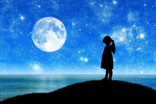 Silhouette, little girl child standing on a hill by the sea looking at the starry sky. Conceptual image of children's dreams